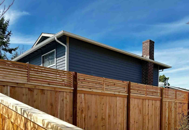 Wooden residential fence installed along a property with a blue house in the background