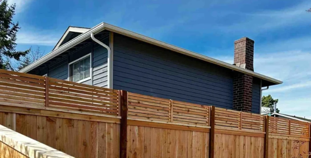Wooden residential fence installed along a property with a blue house in the background